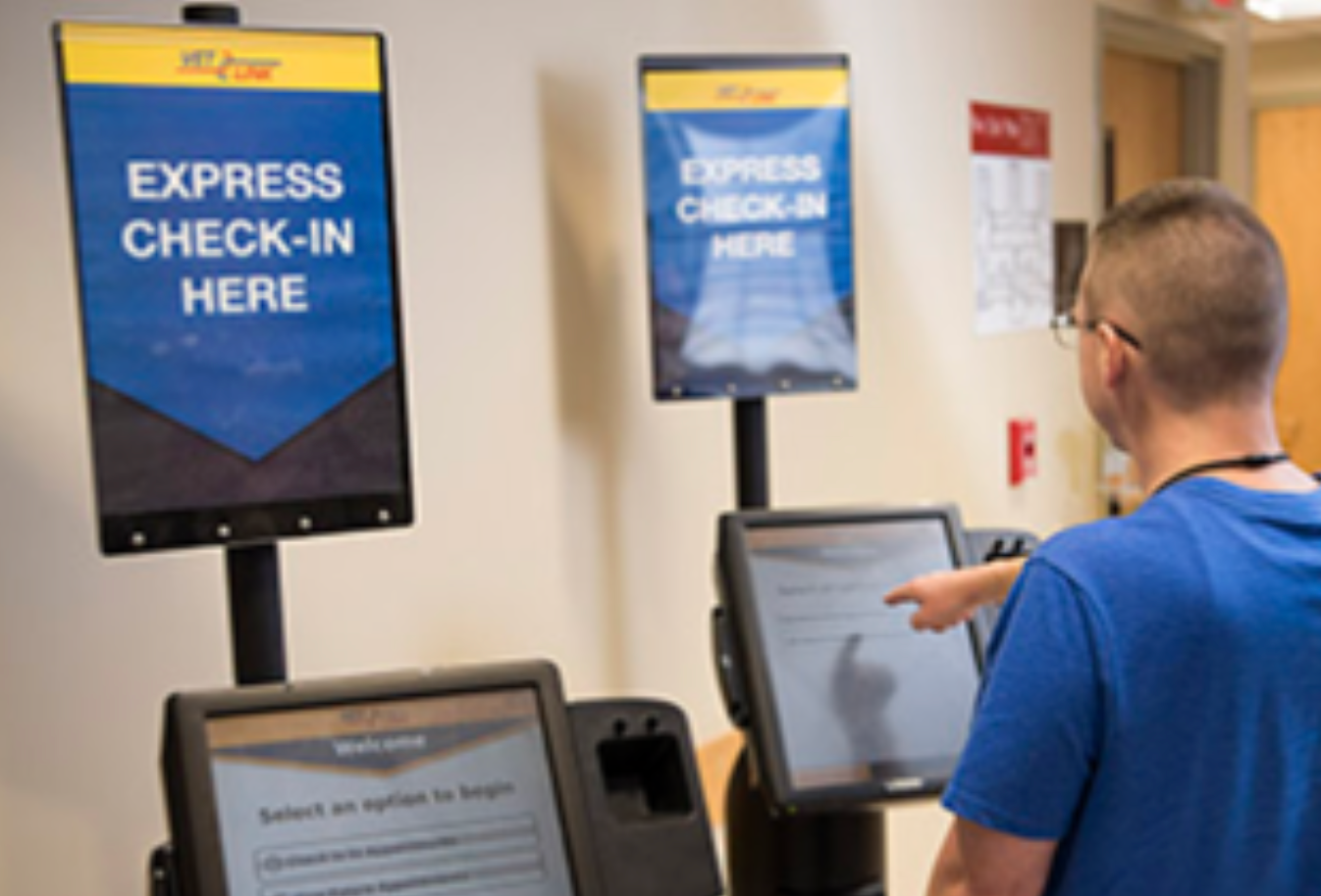 A veteran using an express check-in kiosk with coordinated digital signs mounted above the kiosks